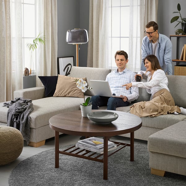Three people chat on beige SÖRVALLEN sofa. Coffee table with bowl and plant in front of large window.