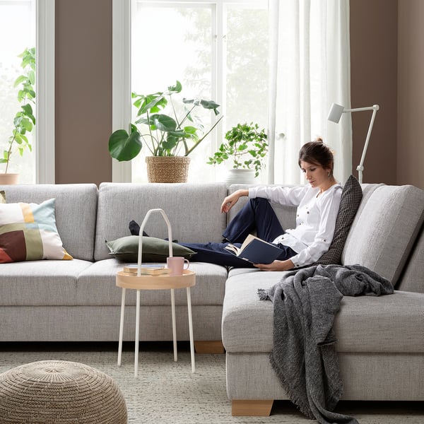 Person reading on grey SÖRVALLEN sofa by window with mug and plants.