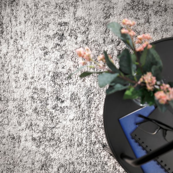 Top view of a grey, round rug with a vase holding pink flowers and green leaves on a table.