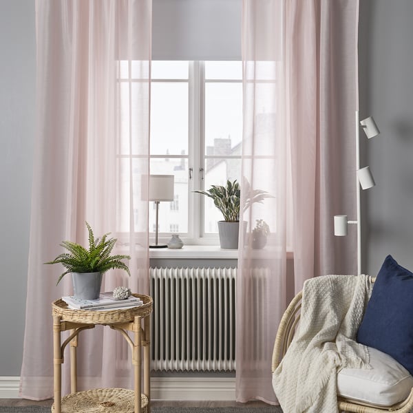 Cozy corner with STENFRÖ sheer pink curtains, a wicker table, and armchair. Curtains softly diffuse light, complementing the modern decor.