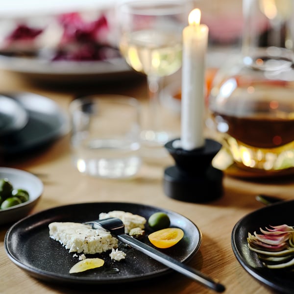 Dark plate with cheese, lemon, olives; candle, glass, bowl beside.