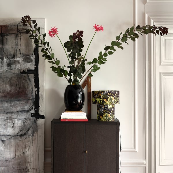 Black oval vase on dark wood cabinet with vibrant flowers; abstract art nearby.
