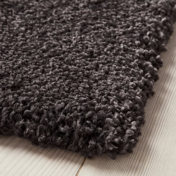 Dark grey shaggy rug, thick and soft pile, lying on light wooden floor.