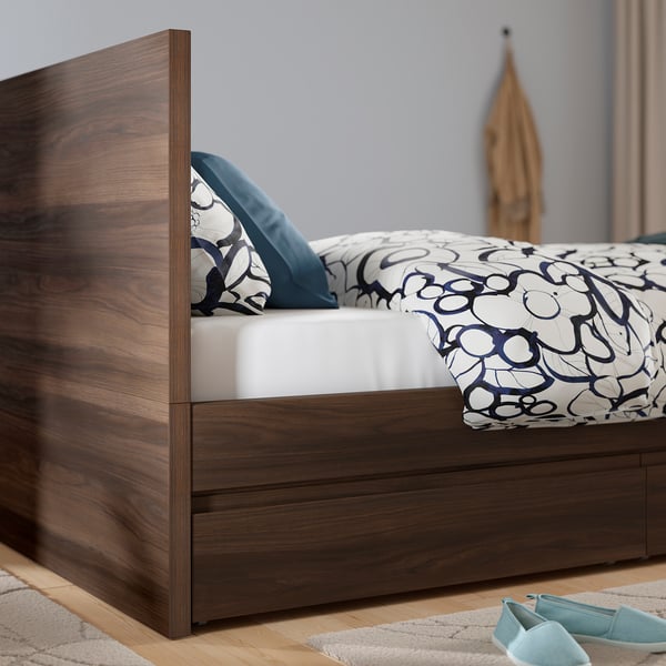 Dark wooden bed frame with drawers and patterned bedding.