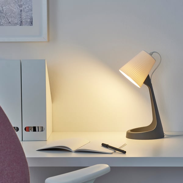 Modern SVALLET lamp on office desk with notebook, folder, and monitor. Wall has framed picture.