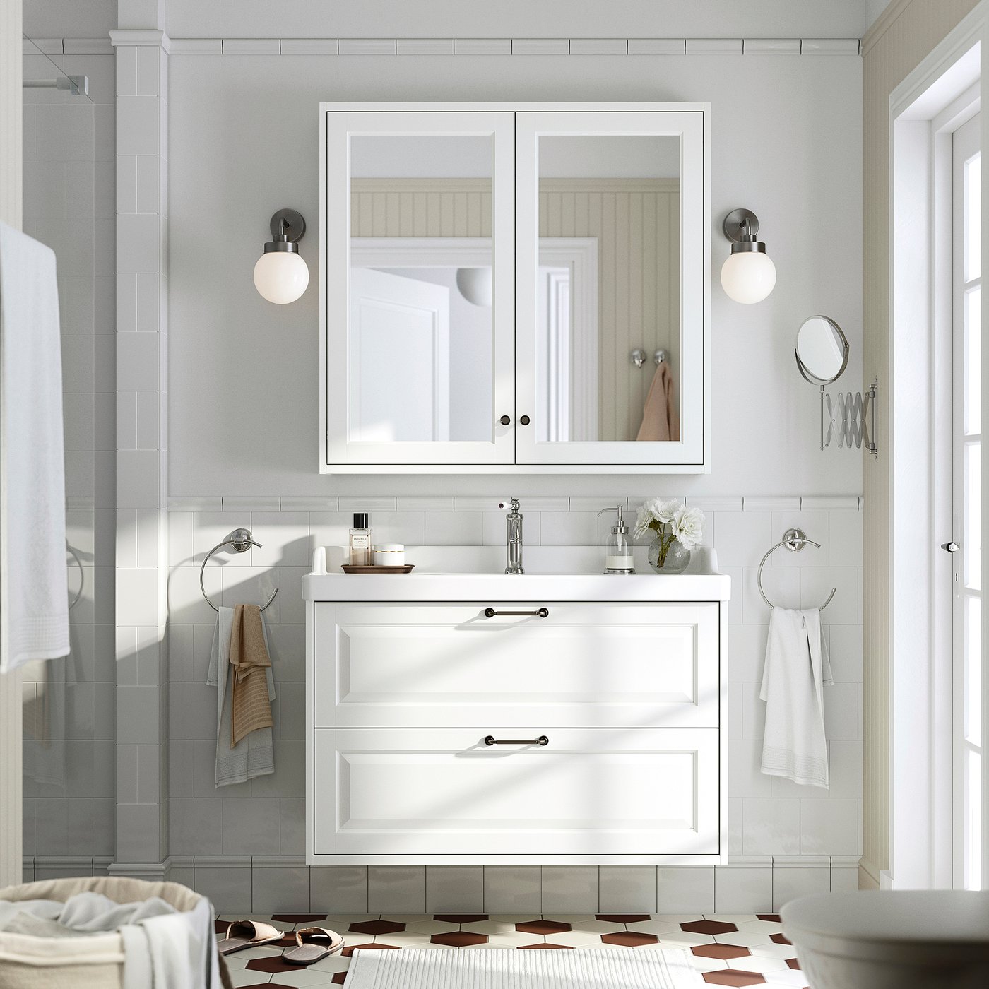 TÄNNFORSEN bathroom: white vanity, mirror cabinet, patterned tiles. Sink flanked by wall lights, towels on silver rings, geometric tile floor.