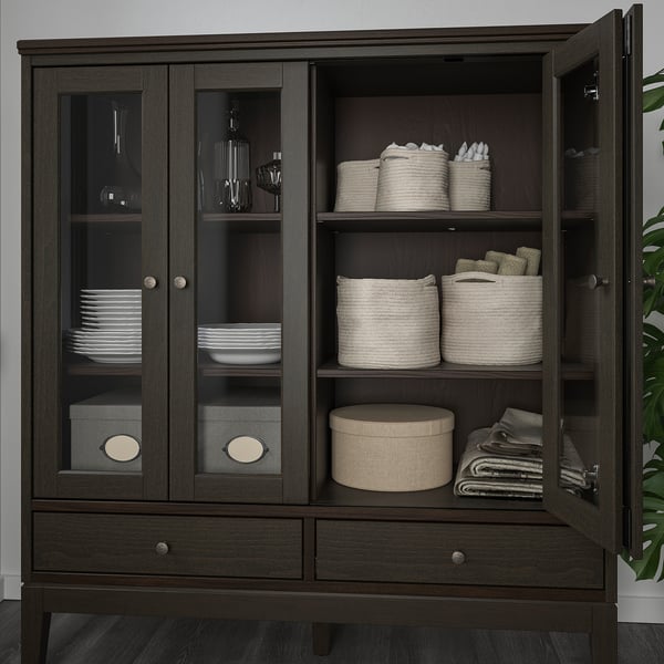 Dark wooden cabinet with glass doors displaying dishes, cutlery, and fabric storage baskets.