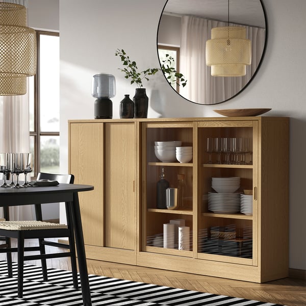 Wooden dining cabinet with sliding doors and cosy light, bowls and glasses inside.