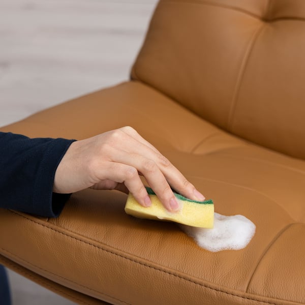 Cleaning couch with yellow sponge, suds, highlighting foaming action.