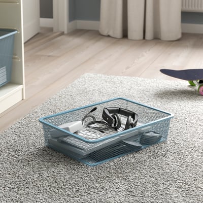 Mesh storage box on carpet, holding headphones and charger, part of TROFAST system.
