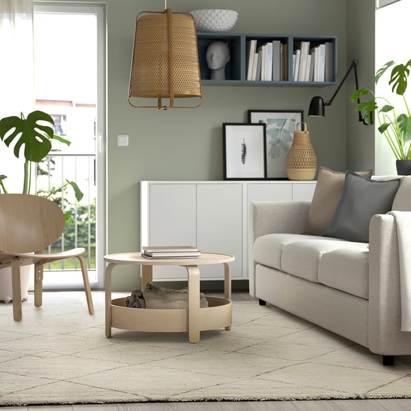 Large rug in neutral tones, green walls, light furniture, coffee table, sofa, chair, plants, modern cosy.
