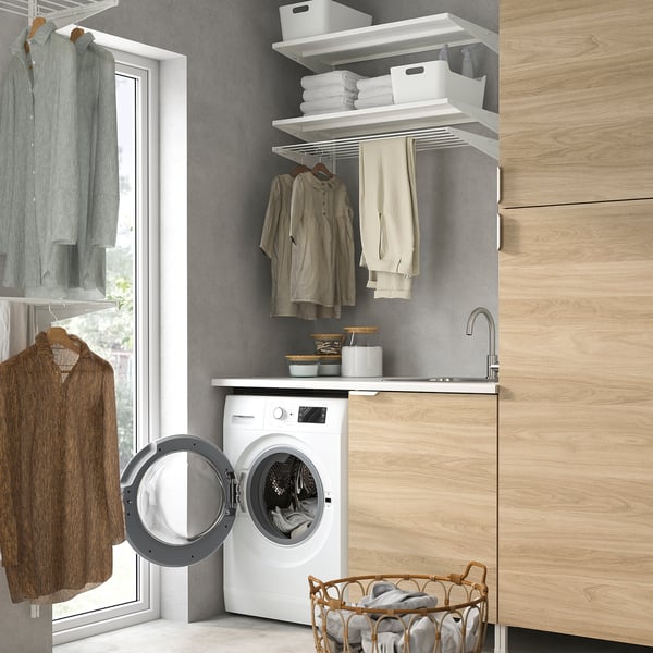 Small laundry room with white UDDARP washer/dryer, open door, wooden shelves with clothes, grey walls.