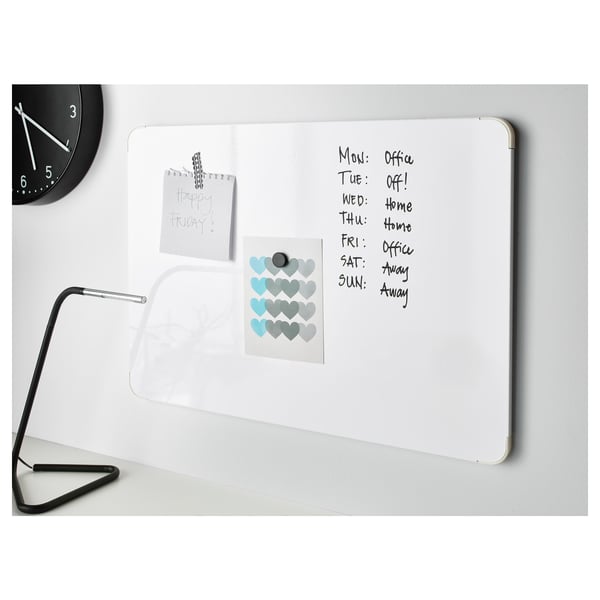 A whiteboard with schedule notes under a clock and lamp, listing days and activities, with stickers and memo.
