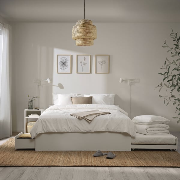 Modern bedroom with white bed, trundle, storage, pendant light, and art frames. Neatly made with white linens and extra pillows. Bright, cosy space.