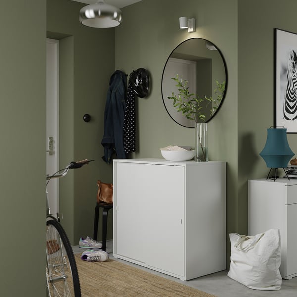 Modern entryway with sage green walls, white ikea VIHALS cabinet, round mirror, hanging coats, and a bicycle.