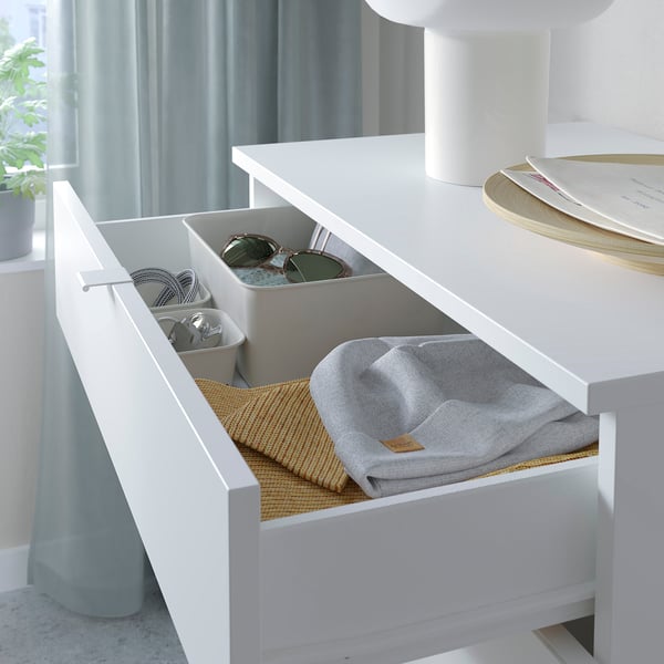 White drawer unit with grey compartments and folded grey cloth inside, organised on a table.