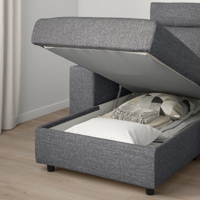 A grey fabric sofa bed with storage compartment open, revealing folded blankets and pillows.