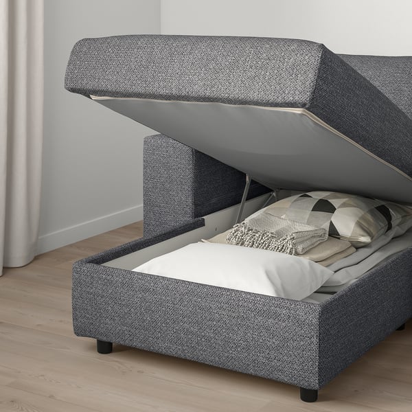 Grey sofa with storage compartment opened, revealing folded bedding inside.