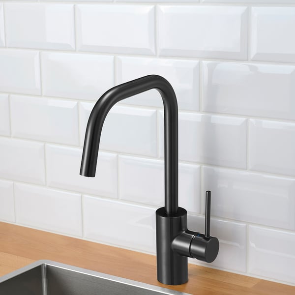 Robinet de cuisine moderne noir avec arche haute et poignée latérale montée sur un comptoir en bois contre un mur carrelé blanc.
