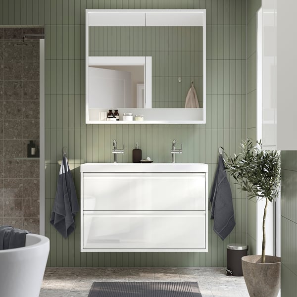 Meuble de salle de bain moderne blanche ÄNGSJÖN avec tiroirs, montée au mur, carreaux verts, miroir, serviettes bleues, plante.