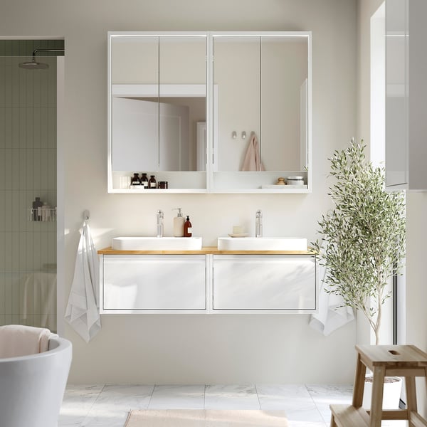 Salle de bain blanche moderne avec lavabo double, meuble miroir, plante.