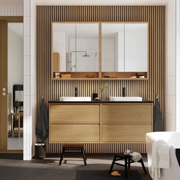 Salle de bain moderne avec vasque en chêne ÄNGSJÖN, grand miroir, deux lavabos et accents noirs. Conception économe en espace, fixée au mur.