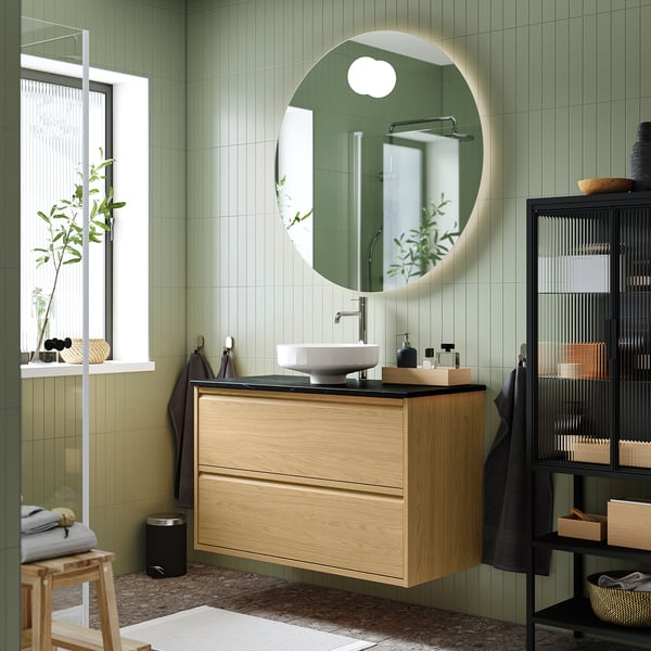 Meuble en chêne élégant avec miroir rond, simple évier, mur carrelé vert.