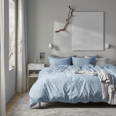 Ensemble de couette ÄNGSLILJA bleu clair dans une chambre confortable à la décoration minimaliste.