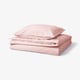 Un ensemble de literie rose soigneusement plié, comprenant une housse de couette et des taies d’oreiller, avec un design décontracté, doux et en coton naturel.