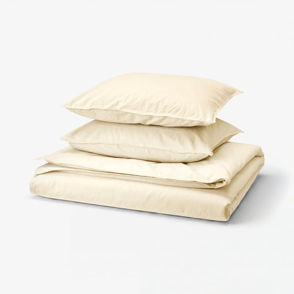 Ensemble de literie en coton crème plié. Comprend une housse de couette, un drap plat et des taies d’oreiller au design classique et simple.