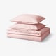 Un ensemble de literie rose nommé ÄNGSLILJA, avec une housse de couette et des taies d’oreiller en coton recyclé et doux. Les articles sont soigneusement pliés et empilés.