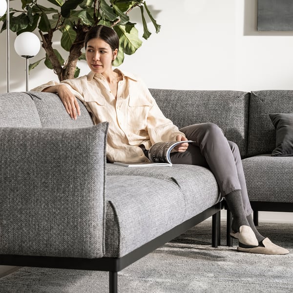 La femme se détend sur un canapé ÄPPLARYD gris moderne, une chemise de couleur claire, un pantalon foncé.