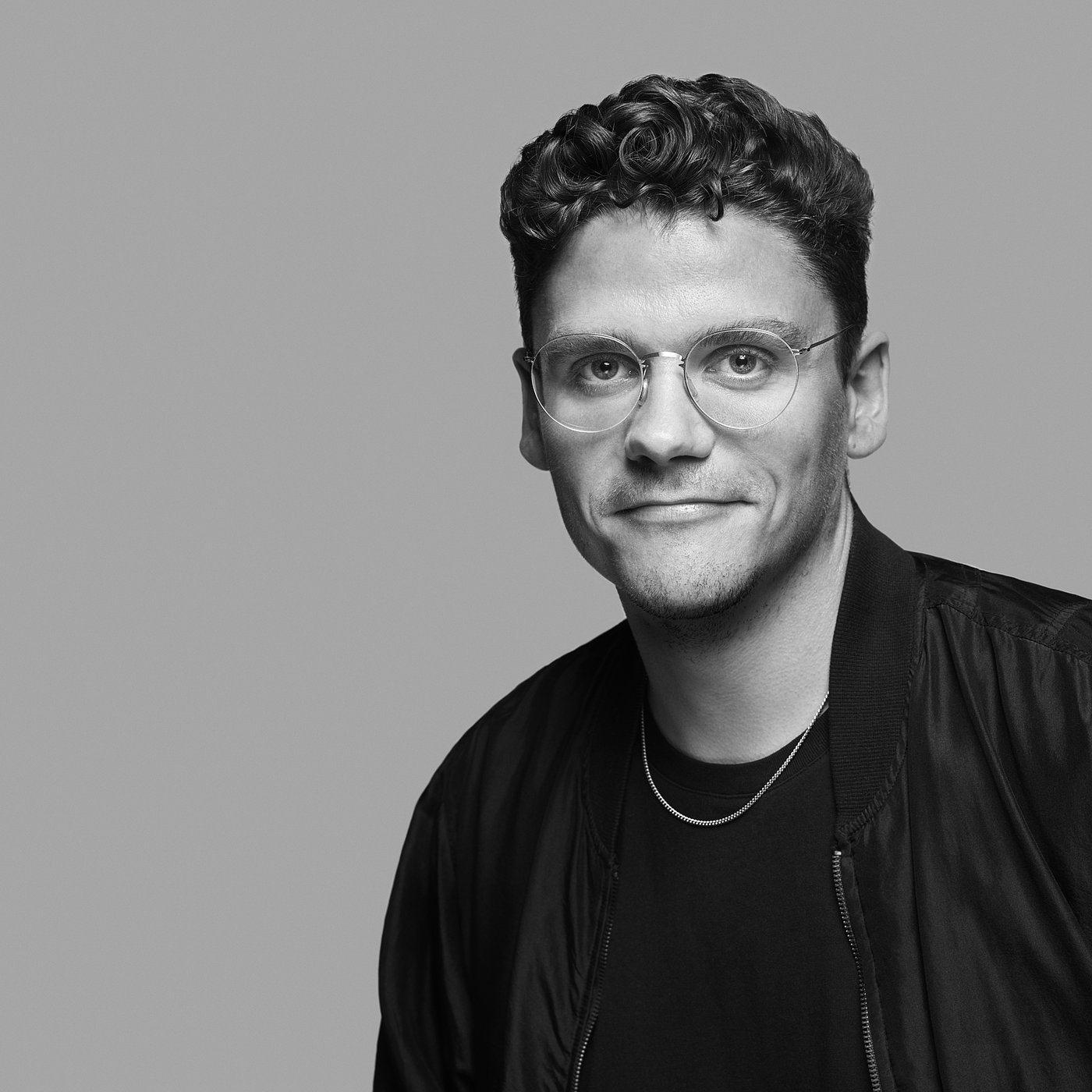 Portrait en noir et blanc de Lukas Bazle portant des lunettes et une veste noire.