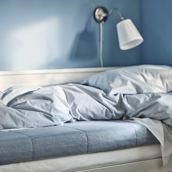 Un matelas en mousse bleue douillet dans une chambre bleue sereine avec une lampe blanche, mettant en valeur son design ferme et confortable.