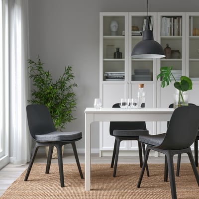 Configuration de salle à manger confortable avec coussin de chaise gris, près de l’étagère, lampe à lumière chaude.