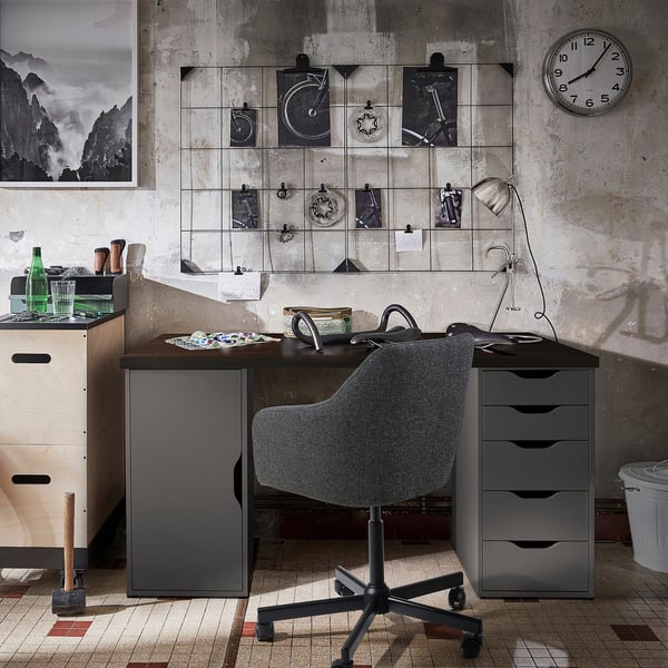 Bureau à domicile industriel ALEX en gris foncé, se fondant avec les tiroirs. Chaise en tissu gris, roulettes noires. Décor moderne avec art mural, horloge.