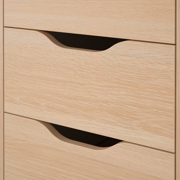 Bureau en bois clair avec trois tiroirs, chacun doté de poignées découpées élégantes, disposées en une ligne verticale soignée.
