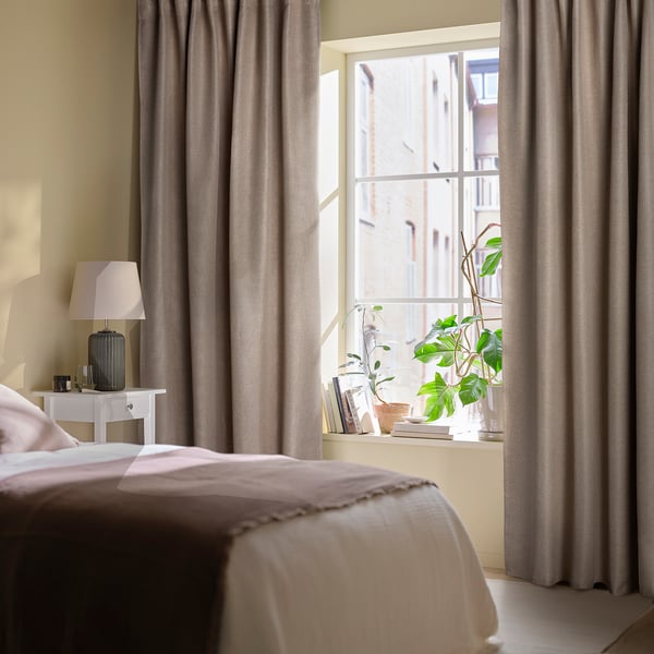 Chambre minimaliste avec rideaux gris ANNAKAJSA , literie blanche, lampe et plante en pot près de la fenêtre.