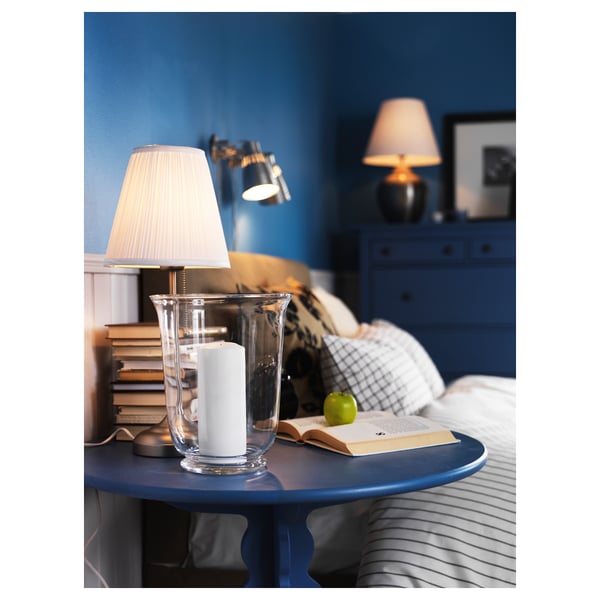 Table de chevet avec lampe allumée, livres, pomme, draps rayés, meubles bleus.