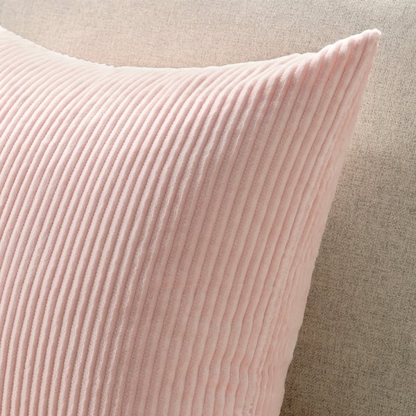 Gros plan d’un coussin en velours côtelé rose pâle doux sur un canapé neutre. La texture est visible, mettant en valeur sa qualité douillette et durable.