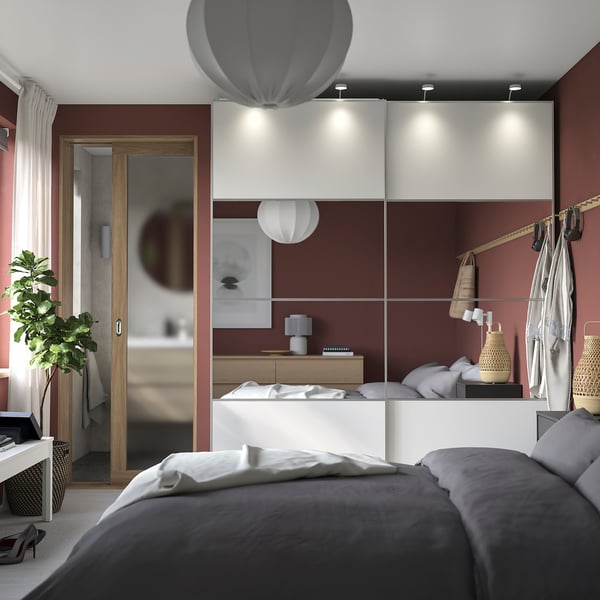 Chambre rouge moderne avec lit gris, lampe de table, armoire à miroir, lampes suspendues et plante.