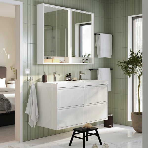Salle de bain moderne avec large lavabo en marbre blanc BACKSJÖN , robinets élégants, grands miroirs, panneaux verts, tabouret noir, plante et serviettes.