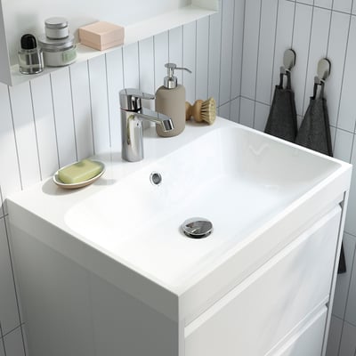 Un lavabo de salle de bain moderne avec robinet chromé, porte-savon et distributeur de savon. Conception en marbre intégrée avec rangement à l’arrière.