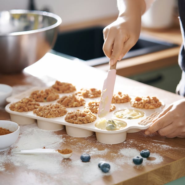 Une personne fait des muffins en utilisant un moule en silicone BAKTIDER . Ils versent la pâte dans des moules avec une spatule. La poêle flexible peut contenir 12 muffins.
