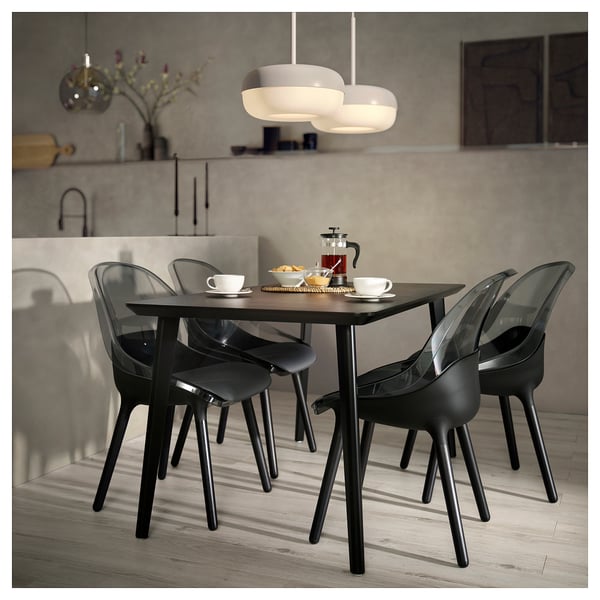 Ensemble de salle à manger moderne avec des chaises sombres et une table en bois, ainsi qu’une lampe suspendue au-dessus.