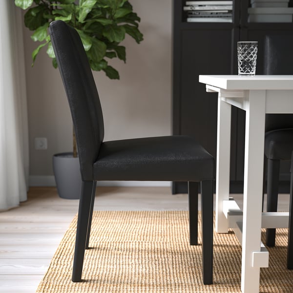 Chaise de salle à manger en cuir noir avec pieds en bois sous une table sur un tapis tissé.