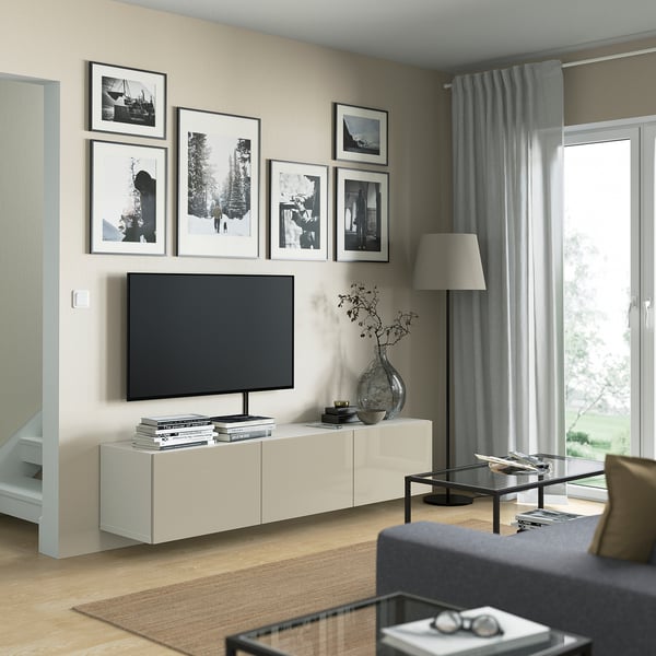Salon moderne avec banc TV BESTÅ, télévision à écran plat, photos en noir / blanc, table basse en verre, canapé gris, grande lampe, grande fenêtre avec rideaux gris.