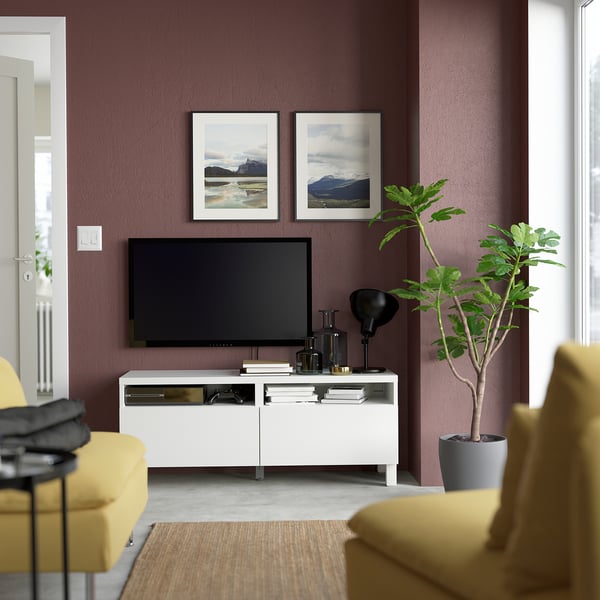 Salon moderne avec des murs violets, un meuble TV BESTÅ blanc, une télévision noire, des chaises jaunes et une grande plante verte.