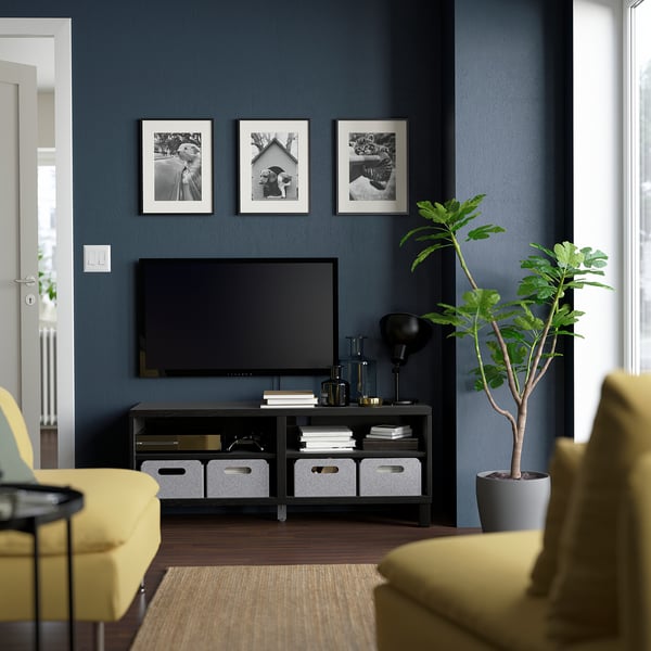 Salon moderne avec banc de télévision BESTÅ, canapé jaune, parquet, mur bleu et plante.
