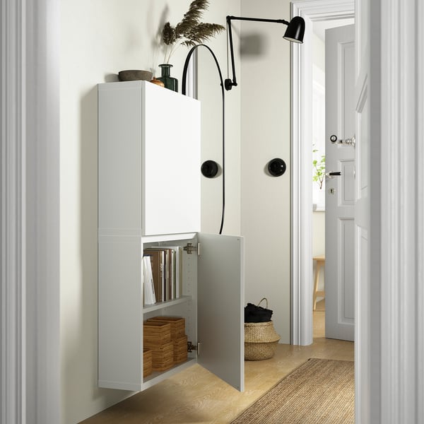 Armoire murale blanche, portes ouvertes laissant voir livres et boîtes, applique murale noire au-dessus.